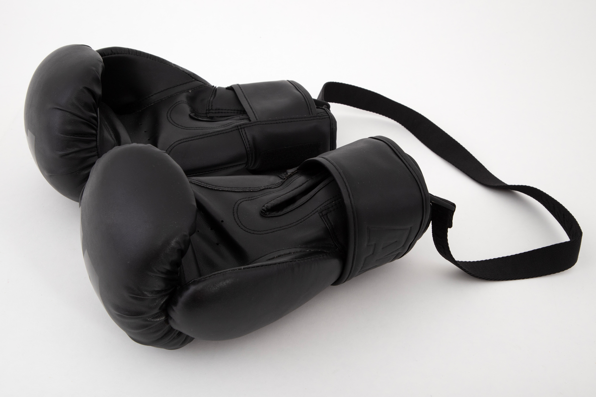 Polstrede og avstivede hansker til bruk ved boksing. Fem små hull i læret sikrer litt ventilasjon inni håndflaten. Lukkes med høy mansjett rundt håndleddet, med åpen splitt på innsiden, ned mot håndflaten. En bred stropp spennes omkring mansjetten og lukkes mot forsiden med like bred borrelås. Denne har bokstavene AW preget inn på forsiden. Ellers har den ene hansken en stor, blank "A" på den knyttede endeflaten, og den andre en tilsvarende "W". Et hull med metallmalje øverst ved splitten på hver hanske brukes til feste for de to krokene i stroppen som binder dem sammen når de ikke er i bruk. Innvendig fôret med syntetisk stoff. Stroppen har navnet WANG vevd inn gjentatte ganger på den ene siden.