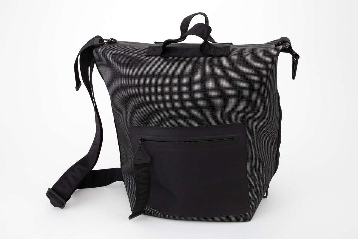 Romslig bag med alternative bæremåter. Enten etter to korte håndtak på øvre kortside, eller etter løkkeformet stropp på enden av øvre kortside, eller etter skulderstropp fra topp til bunn på ene langside. Som skulderbag har sekken også to utforminger: enten bæres den i full størrelse, eller med topp og bunn sammenhektet på motsatt langside. Der er den utstyrt med metallhempe nederst og en slags karabinkrok av metall øverst. Veskens bunn er konstruert med innbrettede kortsider, slik at den ser ut som en konvolutt, og begge langsider og bunnen er forsterket med et svart syntetbånd ivevd gjentatte WANG. Skulderstroppen og alle andre stropper og håndtak er av samme type bånd, de små på toppen en del smalere. Skulderstroppen er dobbel og regulerbar med metallglidestykke merket AW. De to små bærehåndtakene på toppen av bagen er festet på hver side av den gummierte glidelåsen og forsterket med et underliggende bånd av samme type. Bagen er dyp, sydd av et spettet neoprenstoff, svart i bunnfargen og med spetter av sølvfarget, antagelig reflekterende fibre. Alle forsterkningsbånd og stropper er helsvarte. Baggen er fôret med svart nettstoff, og påsydd en stor innerlomme på ene sideveggen. Den er forsterket med smalt bånd av PVC-belagt tekstil og utstyrt med påsydd, matt gummilapp med blank, påtrykt skrift "ALEXANDER WANG X H&M". På for- og baksiden, utvendig, er påsveiset en stor lomme av gummiert tekstil, begge lukket med nesten usynlig, fastsveiset glidelås.