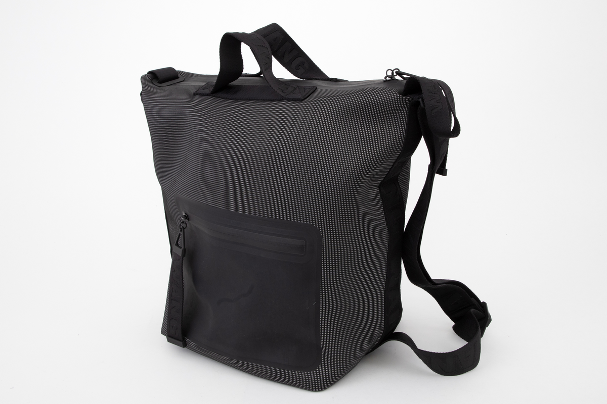 Romslig bag med alternative bæremåter. Enten etter to korte håndtak på øvre kortside, eller etter løkkeformet stropp på enden av øvre kortside, eller etter skulderstropp fra topp til bunn på ene langside. Som skulderbag har sekken også to utforminger: enten bæres den i full størrelse, eller med topp og bunn sammenhektet på motsatt langside. Der er den utstyrt med metallhempe nederst og en slags karabinkrok av metall øverst. Veskens bunn er konstruert med innbrettede kortsider, slik at den ser ut som en konvolutt, og begge langsider og bunnen er forsterket med et svart syntetbånd ivevd gjentatte WANG. Skulderstroppen og alle andre stropper og håndtak er av samme type bånd, de små på toppen en del smalere. Skulderstroppen er dobbel og regulerbar med metallglidestykke merket AW. De to små bærehåndtakene på toppen av bagen er festet på hver side av den gummierte glidelåsen og forsterket med et underliggende bånd av samme type. Bagen er dyp, sydd av et spettet neoprenstoff, svart i bunnfargen og med spetter av sølvfarget, antagelig reflekterende fibre. Alle forsterkningsbånd og stropper er helsvarte. Baggen er fôret med svart nettstoff, og påsydd en stor innerlomme på ene sideveggen. Den er forsterket med smalt bånd av PVC-belagt tekstil og utstyrt med påsydd, matt gummilapp med blank, påtrykt skrift "ALEXANDER WANG X H&M". På for- og baksiden, utvendig, er påsveiset en stor lomme av gummiert tekstil, begge lukket med nesten usynlig, fastsveiset glidelås.