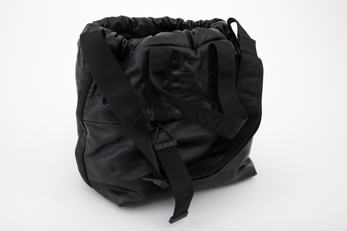 Posete bag av mykt skinn, åpen øverst, men kan lukkes med tykk snor i løpegang. Snoren dras til og stoppes med en "gummihylse". Skulderstroppen er av kraftig, dobbelvevd syntetbånd ivevd WANG. Den kan reguleres ved hjelp av glidespenne i gummiert metall, merket AW, og er fastsydd over sidesømmen helt ned på hver side av vesken. I tillegg har den korte bærehåndtak på for- og bakstykket, festet halveis ned på hver flate. Front- og bakstykket er sammensydd av en øvre og nedre del og skjult i sømmen er det en glidelåslomme på begge sider. Innvendig er det et stort hovedrom. I tillegg er påsydd to mindre lommer på den ene siden og et større glidelåsrom på den andre siden. De utvendige glidelåsene er utstyrt med kraftig drastropp festet i glideren. Denne er av samme bånd ivevd WANG. Vesken er innvendig fôret med nettstoff. Alle lommer og ekstrarom er også sydd av samme nettstoff. Innvendig plate innsydd i veskebunnen, og i tillegg en påsydd gummiplate utvendig, med fire ben av bokstavene AW i høyt relieff.