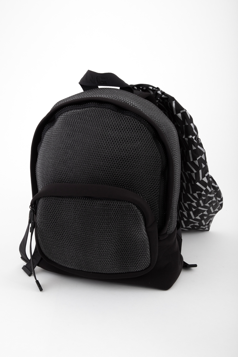 Liten sekk for trening. Sydd av nettstoff, der det ytre stoffet er laminert med flere lag nettstoff, og kjernen antagelig selvlysende, dvs av lysegrå refleksfibre. Sekken består av ett hovedrom og et lite ytterrom. Nedre del av både sekk og ytterrom er av tett neopren. Selve bunnen har en påsydd plate av gummi, med 4 "ben" i form av logoen "AW".  Innvendig bunnplate er imidlertid både bredere og lengre og av ukjente materiale. Sekken er flat nederst og buet i overkant, hovedrommet åpnes nesten helt ned i begge sider og lukkes med grov plastglidelås. Ytterommet åpnes i overkant og lukkes med tilsvarende glidelås. Innvendig er rommene fôret med et ekstra lag, enkelt nettstoff, og hovedrommet utstyrt med en ekstra lomme. Selene er regulerbare med spenner, er polstret, av neopren og utvendig forsterket med påsydde bånd av bevernylonlignende materiale ivevd "WANG" gjentatte ganger. Tilsvarende stropp øverst, til bæring i hånden. Under selefestene en ekstra lomme, lukket med samme grove glidelåstype. Nedi lommen ligger et påsydd regntrekk av tynt, vannavstøtende matriale, med påtrykt "AW" i et sammenhengende mønster utført i lysreflekterende trykkfarge over det hele. Med påsydd elastikk langs ytterkanten, kan trekket raskt tas ut og vikles omkring sekkens front og holde seg på plass i regnvær. Alle glidelåser er utstyrt med en "drastropp" av det sorte båndet ivevd WANG.