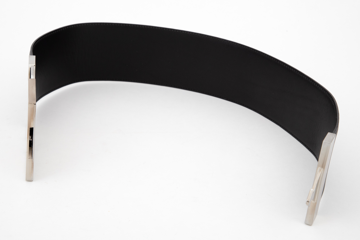 Kraftig, stivt og bredt lærbelte, laminert av to lag og randsydd. Stor beltespenne av børstet stål. Låses ved at en pilformet tapp på det ene, smale beslaget skyves inn i den store "platen", en slags "låskasse", på motsatt side. For å løse ut tappen må to sidetapper på den store platen trykkes inn samtidig. Forsiden på beltespennen er helt glatt, men børstet, mens alle festeskruene kan sees på baksiden. Tilsammen 9 små stjerneskruer fordelt på låsens to endestykker.