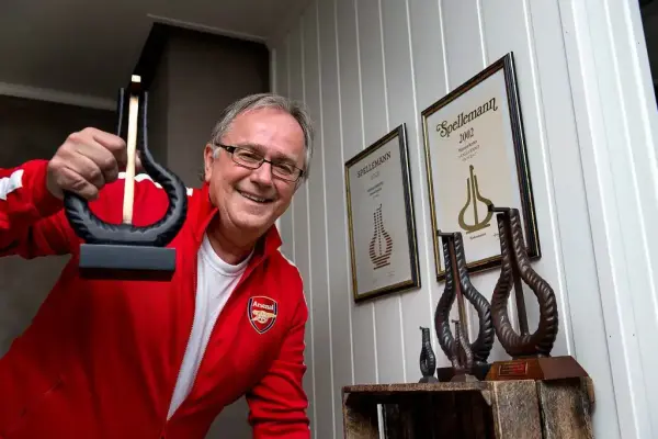 Musiker Arnstein Tungvåg med rød Arsenal-supporterjakke holder opp en Spellemannpris. På ei hylle bak ham står to priser til. 