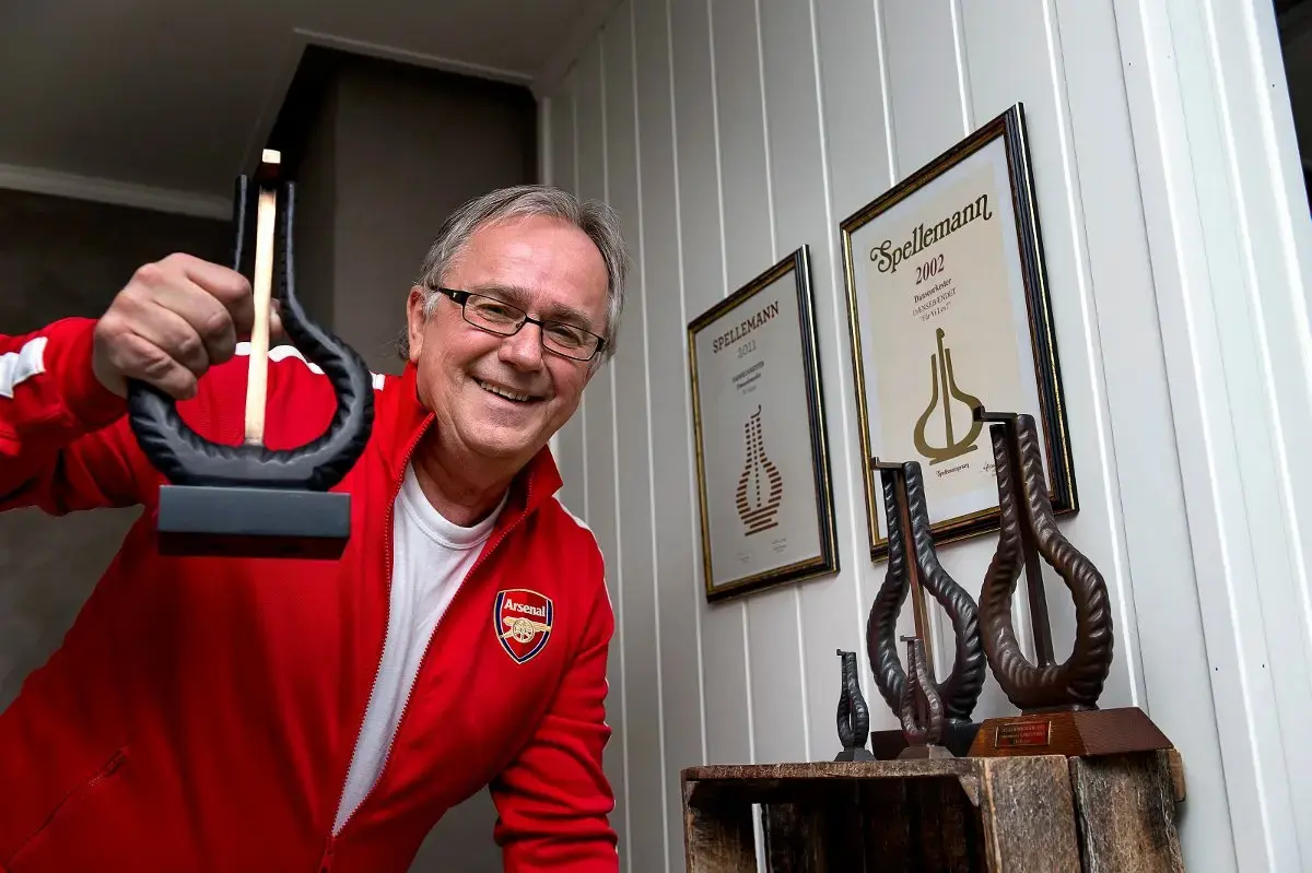 Musiker Arnstein Tungvåg med rød Arsenal-supporterjakke holder opp en Spellemannpris. På ei hylle bak ham står to priser til. 
