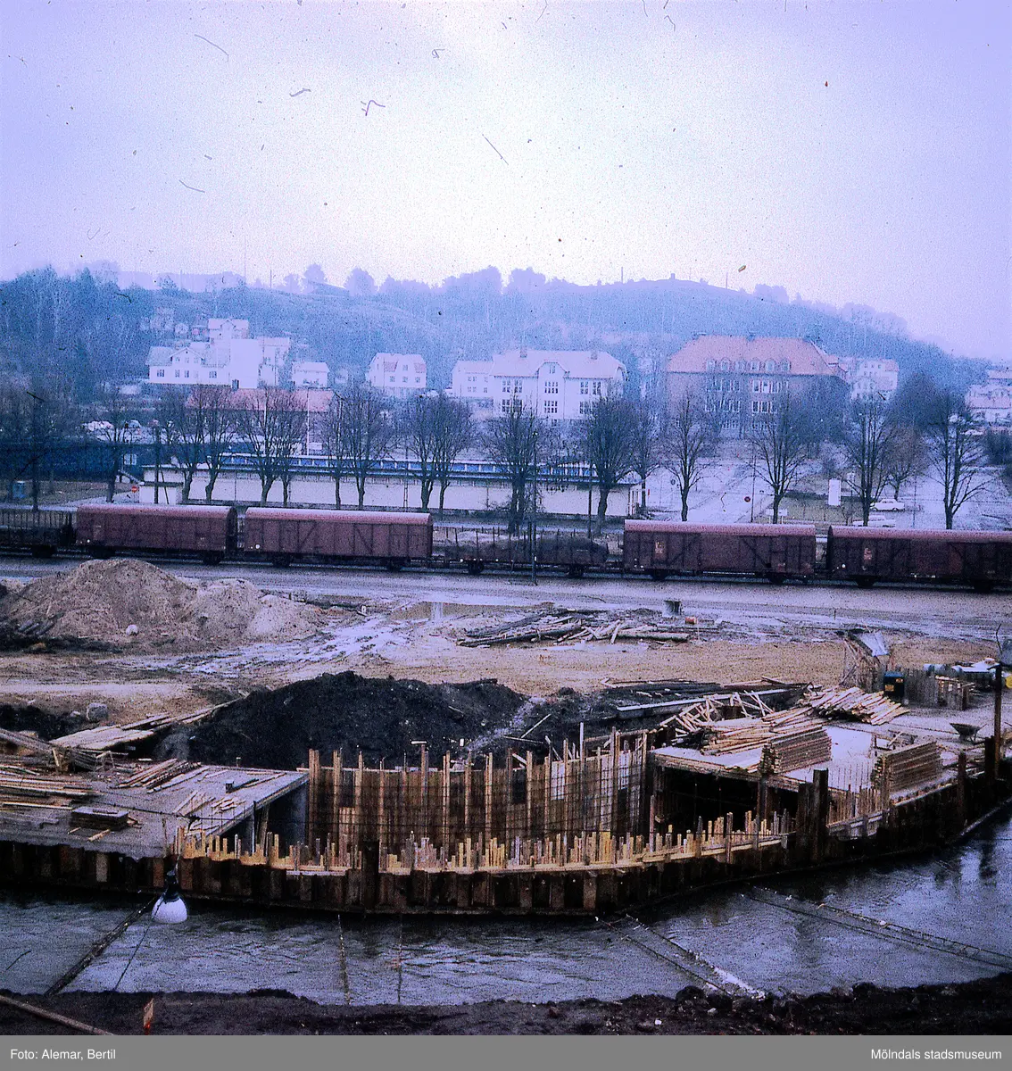 Muddring av Mölndalsån inför planerad byggnation av Mölndals bro. Tid: Omkring 1974. I bakgrunden syns Träskolan, Nya Torget och stadsdelen Trädgården. Kvarnbyskolan syns till vänster i bild.
I bakgrunden till vänster, skymtar bergen där idrottsanläggningen Kvarnbyvallen ligger.