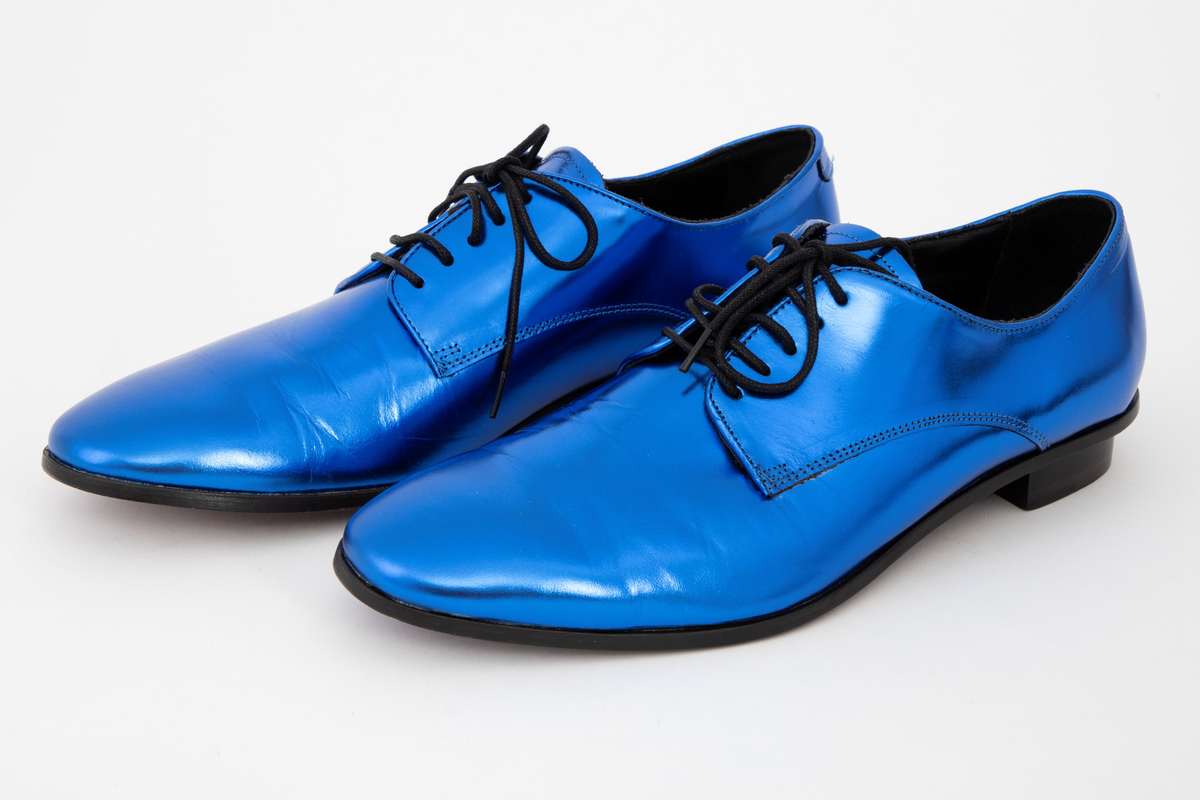 Herresko, metallisk blå, avrundet foran med fem hull på hver side og rund svart lisse. Lav hæl med svart kant rundt skoen.