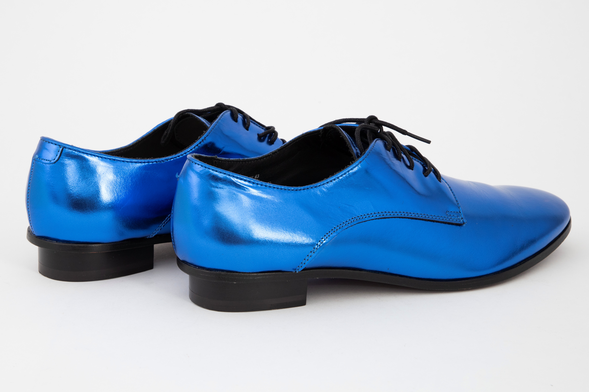 Herresko, metallisk blå, avrundet foran med fem hull på hver side og rund svart lisse. Lav hæl med svart kant rundt skoen.