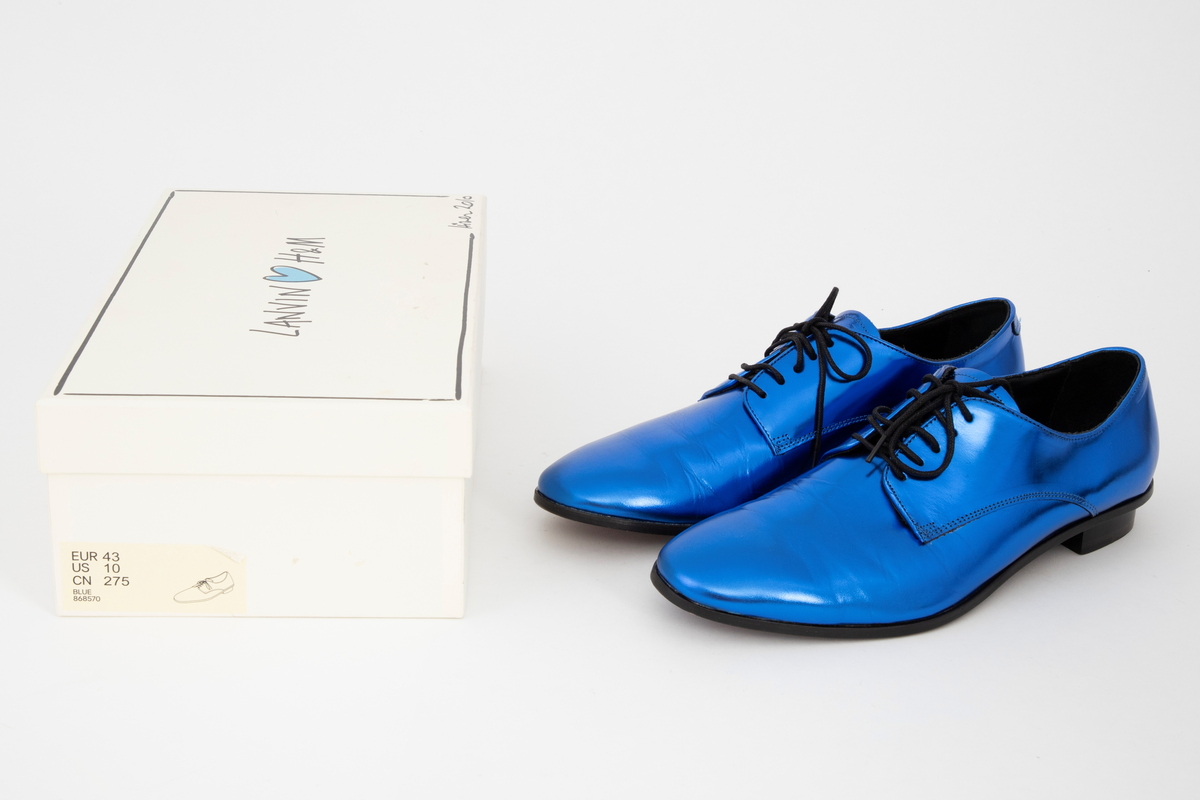 Herresko, metallisk blå, avrundet foran med fem hull på hver side og rund svart lisse. Lav hæl med svart kant rundt skoen.