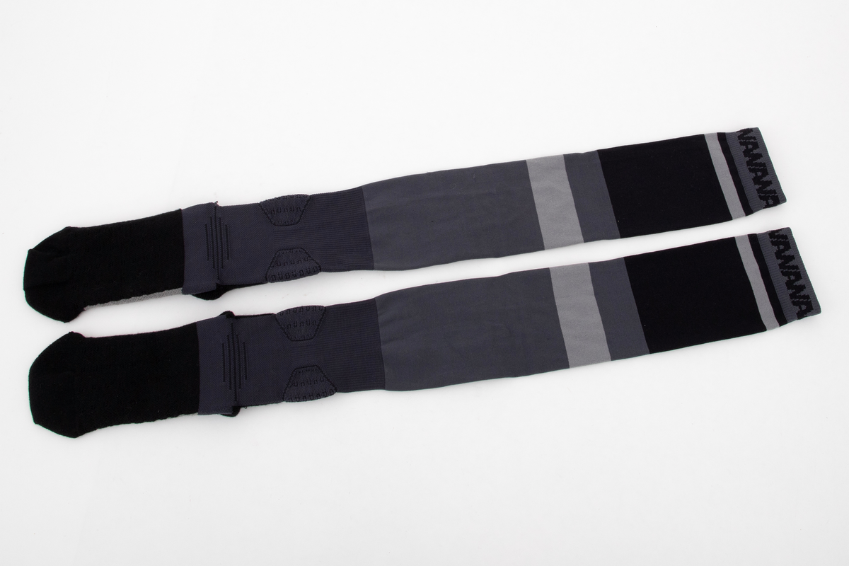 Et par trange og svært elastiske strømper. Innvendig frotté i såle og hæl og ved hvert ankelledd. Ulike strikketeknikker i såle, over vrist og ved ankelledd gir ulik grad effekt av beskyttelse mot press og ulik grad av kompresjon. Navnet WANG er strikket inn med boksstavene vertikalt stilt på baksiden av leggen, og bokstavene AW er dradd sammen og parstilt under sålen. I tillegg er bokstavene AW fortløpende strikket inn på yttersiden av den doble vrangborden. Bokstavene er flosset, dvs trådene avkuttet og tovet, i konturen på vrangen, dvs at det ikke er løpende tråder i mønsteret. Strikket i ulike nyanser grått, i horisontale striper av ulik bredde.