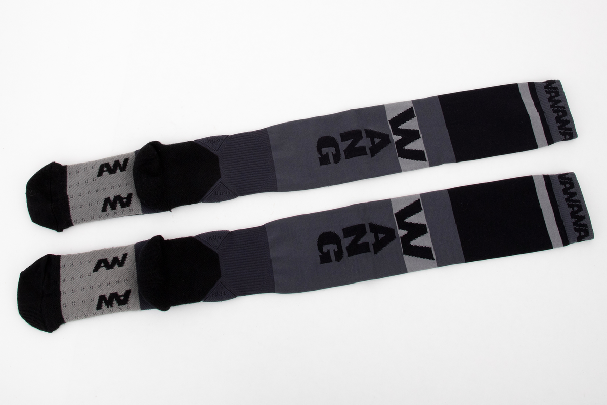 Et par trange og svært elastiske strømper. Innvendig frotté i såle og hæl og ved hvert ankelledd. Ulike strikketeknikker i såle, over vrist og ved ankelledd gir ulik grad effekt av beskyttelse mot press og ulik grad av kompresjon. Navnet WANG er strikket inn med boksstavene vertikalt stilt på baksiden av leggen, og bokstavene AW er dradd sammen og parstilt under sålen. I tillegg er bokstavene AW fortløpende strikket inn på yttersiden av den doble vrangborden. Bokstavene er flosset, dvs trådene avkuttet og tovet, i konturen på vrangen, dvs at det ikke er løpende tråder i mønsteret. Strikket i ulike nyanser grått, i horisontale striper av ulik bredde.