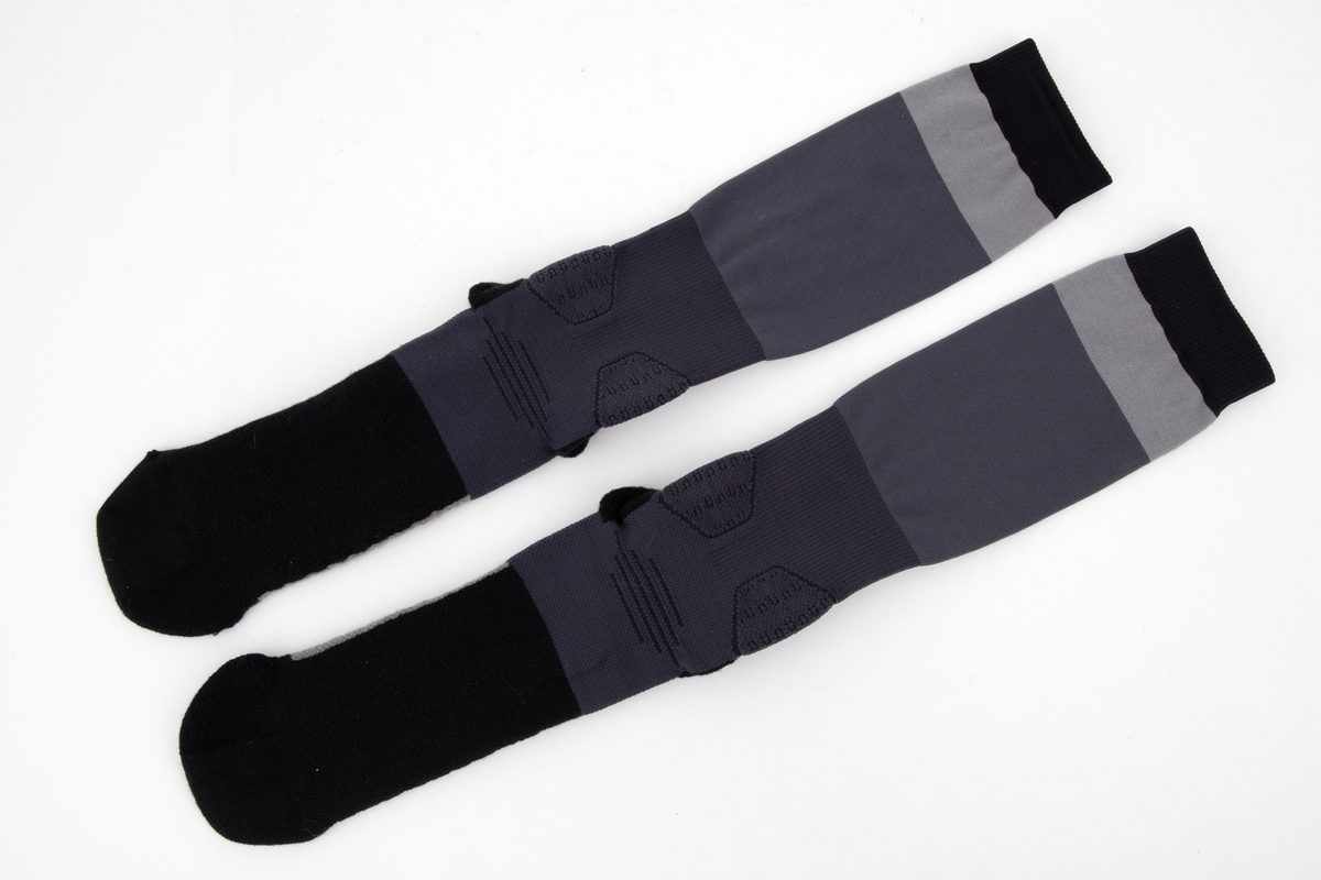 Et par trange og svært elastiske strømper. Innvendig frotté i såle og hæl og ved hvert ankelledd. Ulike strikketeknikker i såle, over vrist og ved ankelledd gir ulik grad effekt av beskyttelse mot press og ulik grad av kompresjon. Navnet WANG er strikket inn med boksstavene vertikalt stilt på baksiden av leggen, og bokstavene AW er dradd sammen og parstilt under sålen. Bokstavene er flosset, dvs trådene avkuttet og tovet, i konturen på vrangen, dvs at det ikke er løpende tråder i mønsteret. Strikket i ulike nyanser grått, i horisontale striper av ulik bredde.