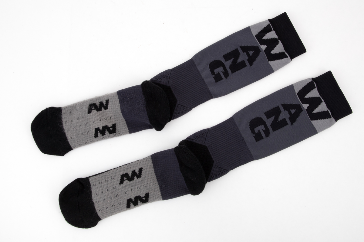 Et par trange og svært elastiske strømper. Innvendig frotté i såle og hæl og ved hvert ankelledd. Ulike strikketeknikker i såle, over vrist og ved ankelledd gir ulik grad effekt av beskyttelse mot press og ulik grad av kompresjon. Navnet WANG er strikket inn med boksstavene vertikalt stilt på baksiden av leggen, og bokstavene AW er dradd sammen og parstilt under sålen. Bokstavene er flosset, dvs trådene avkuttet og tovet, i konturen på vrangen, dvs at det ikke er løpende tråder i mønsteret. Strikket i ulike nyanser grått, i horisontale striper av ulik bredde.