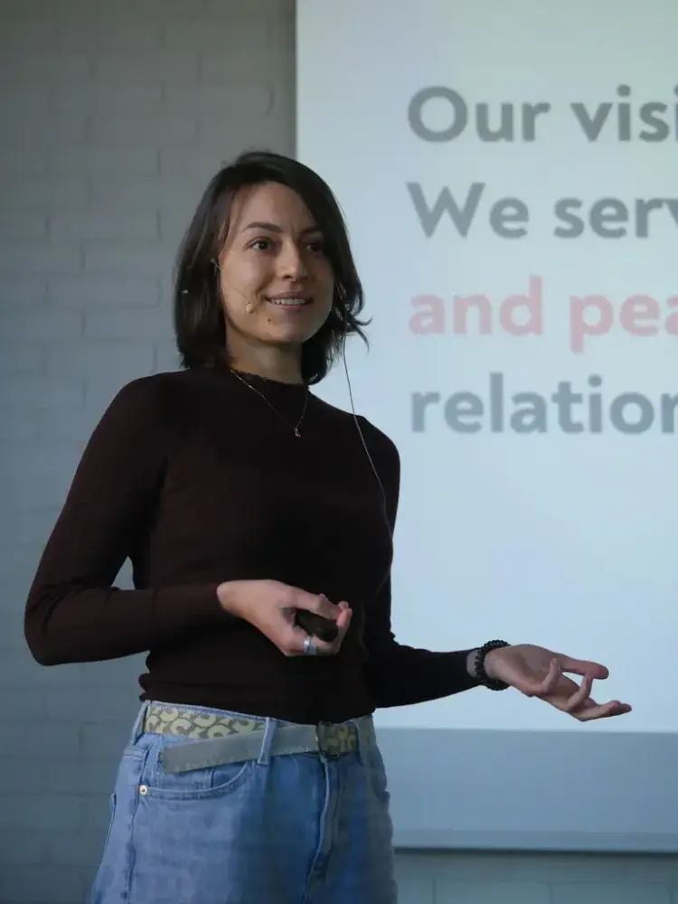 En kvinne med sort genser står foran en skjerm med deler av en engelsk tekst på.