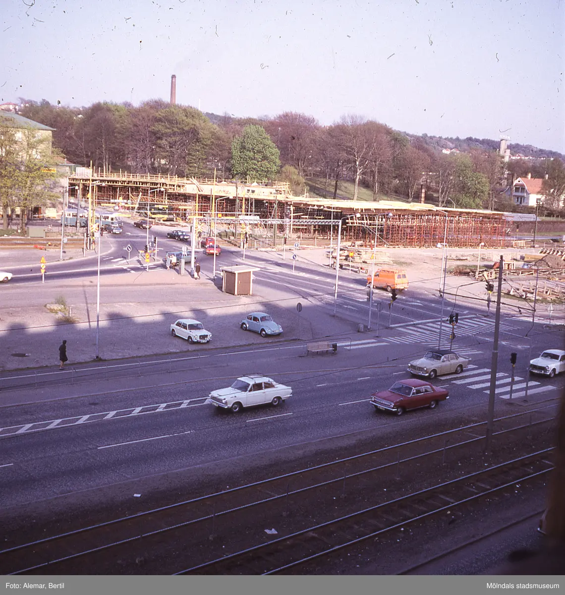 Långt framskriden byggnation av Mölndals bro, ser ut att vara taget under någon gång i slutet på våren eller i början av sommarmånaderna juni till augusti.
Tid: Cirka början av 1970-talet. 
Bilden visar stadstrafik samt anläggningsarbete. 
I bakgrunden skymtar den stora skorstenen som finns vid den här tiden på Papyrus område. Dessutom syns tornet med företagsnamnet Papyrus, långt bort till höger i bakgrunden. 
I förgrunden syns flertalet personbilar parkerade.
Längst ned till höger skymtar spårgvagnsspåren.