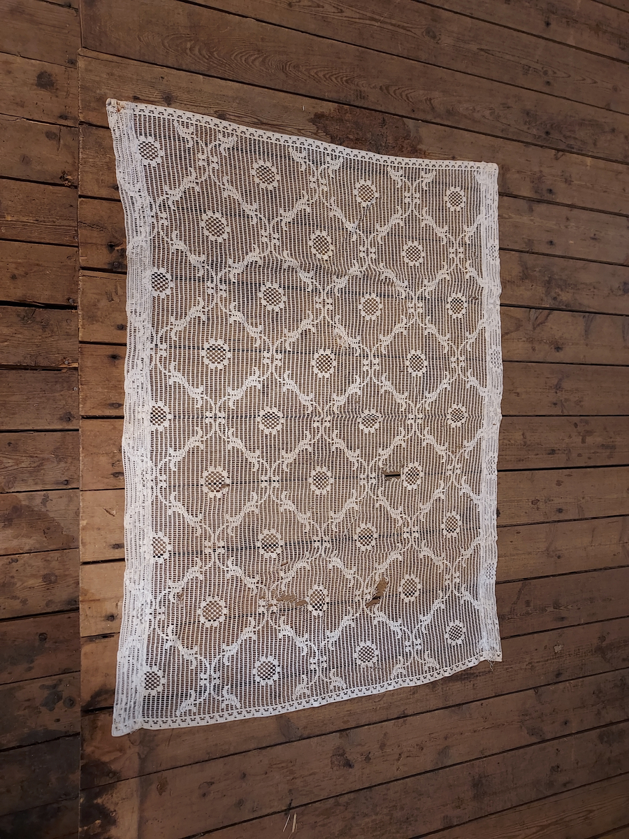 Gardin. Hvit. Bomull. Blonde gardin med blomsterorn. Oppbrett til oppheng på begge langsider. Noe defekt.