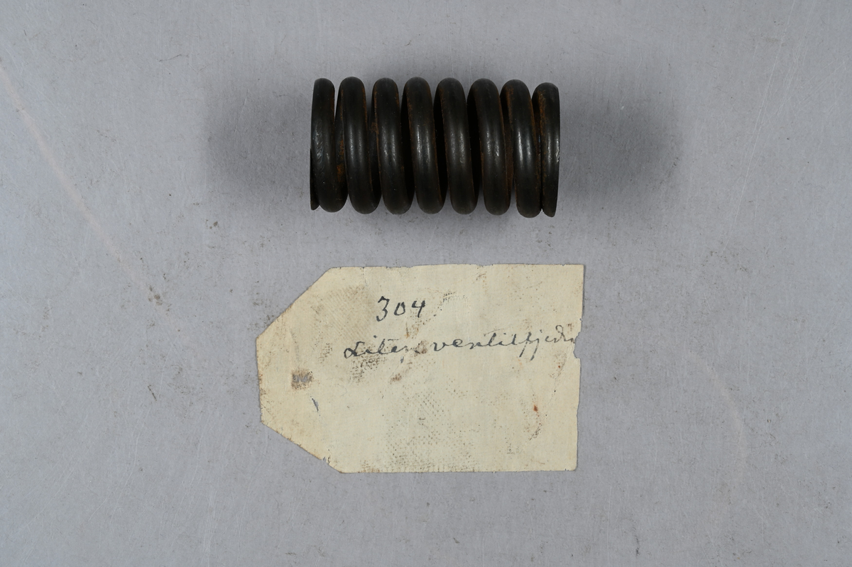 Sju prover på ventilspiralfjäder i olika storlekar. Sex av proverna även märkt med egen etikett med märkning 303-308. Tillhörande lapp med notering: "Diverse ventilspiralfjädrar för explosionsmotorer. Från A-B. Spiralfabriken."