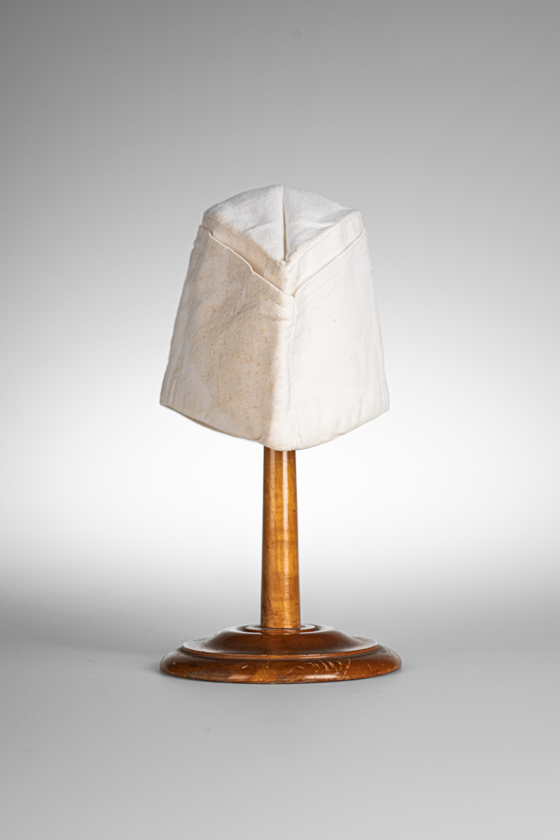 Vii, avlång mössa i bomullstyg. Stämpel med texten "KRONOBAGERIET" på båda sidorna inuti mössan. Märkt med etikett och texten "Fristads S C 58 -SANFORD" i blå text.