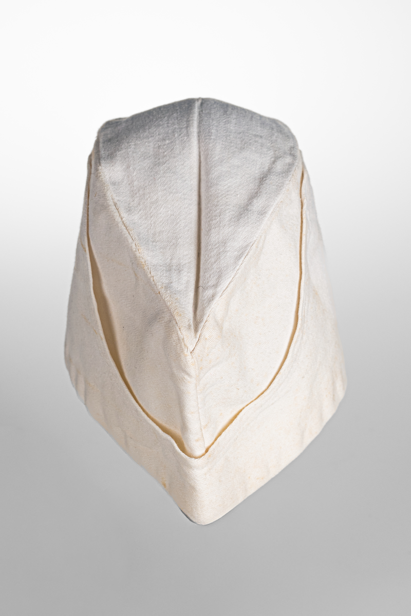 Vii, avlång mössa i bomullstyg. Stämpel med texten "KRONOBAGERIET" på båda sidorna inuti mössan. Märkt med etikett och texten "Fristads S C 58 -SANFORD" i blå text.