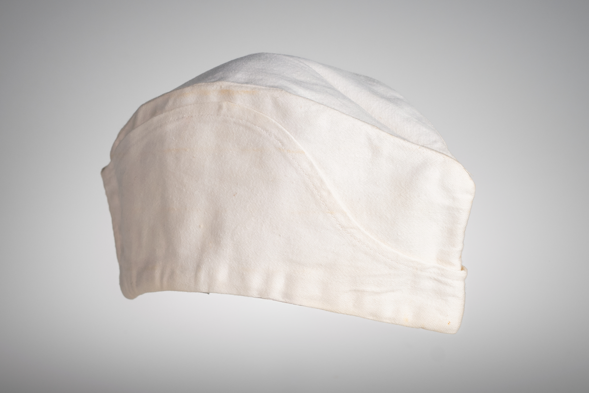 Vii, avlång mössa i bomullstyg. Stämpel med texten "KRONOBAGERIET" på båda sidorna inuti mössan. Märkt med etikett och texten "Fristads S C 58 -SANFORD" i blå text.