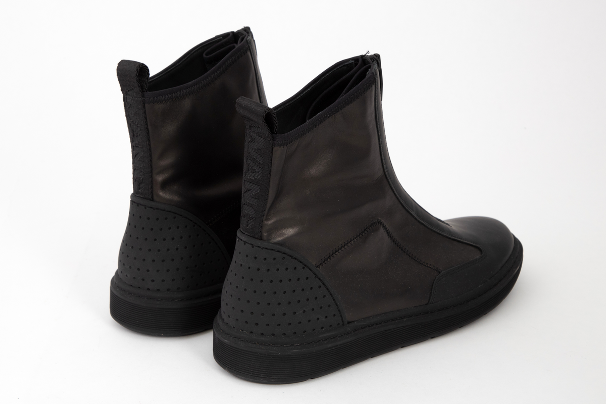 Ankelhøye herrestøvler i svart skinn med kraftig, svart glidelås midt foran. På baksiden påsydd bånd med hempe øverst og innvevd logo: WANG. Kraftig profilert såle med bokstavene WA etter hverandre.