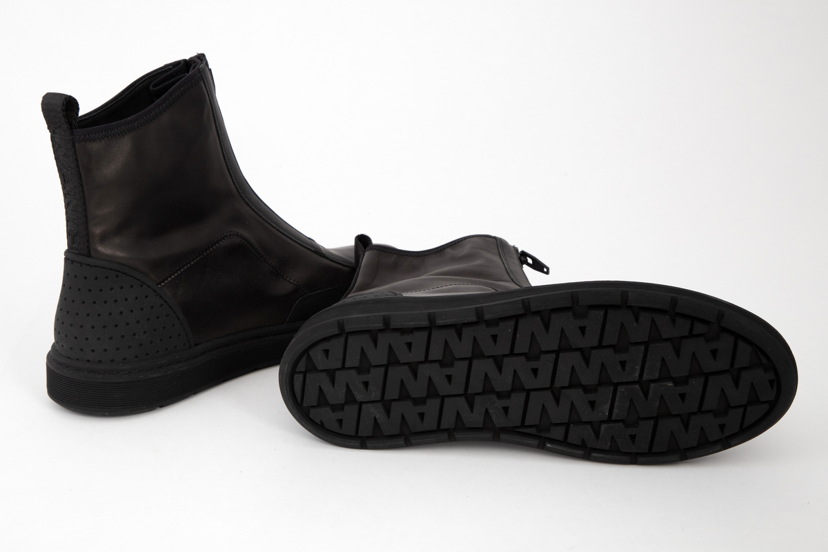 Ankelhøye herrestøvler i svart skinn med kraftig, svart glidelås midt foran. På baksiden påsydd bånd med hempe øverst og innvevd logo: WANG. Kraftig profilert såle med bokstavene WA etter hverandre.
