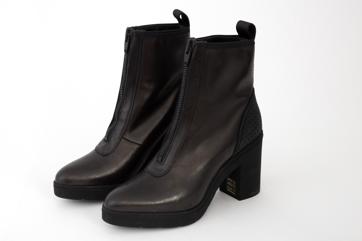 Ankelhøye damestøvletter i svart skinn med kraftig, svart glidelås midt foran. På baksiden påsydd bånd med hempe øverst og innvevd logo: WANG. Kraftig, kantete hæl og profilert såle med bokstavene WA etter hverandre.