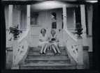 Två unga kvinnor, Elsa t.h., med en hund emellan sig, sitter på trappan till  familjen Morthensens villa Solveden, Djursholm.