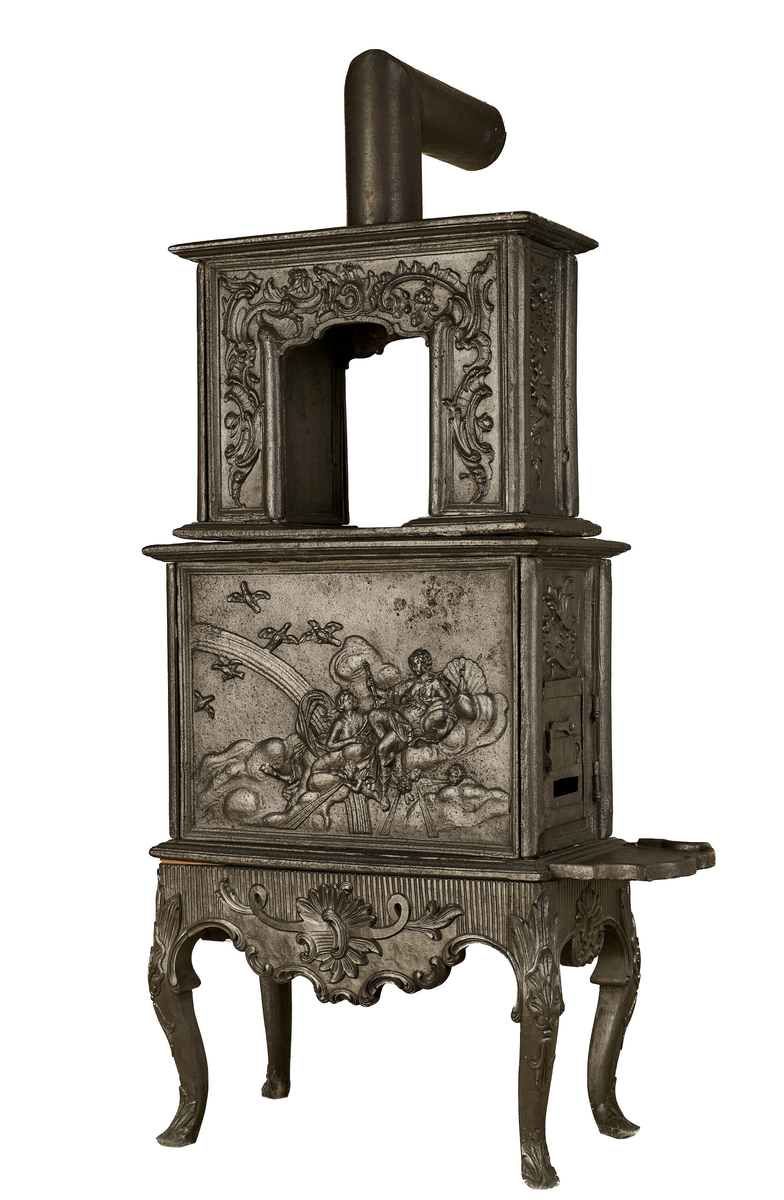 Ovn i to etasjer, utført i støpejern. Den bæres av en trebase med rokokkoornamentikk på midten av sargen, samt svungne capriolben. Samtlige sider er riflet, og innrammet av listverk og profiler. Frontpanelet på nedre del viser en fremstilling av Iris som overbringer et budskap til Juno, omgitt av skyer, regnbue og amoriner som blåser i trompeter. Til venstre flyver Junos gjess. Det høyre sidefeltet har ovnsluke og askebrett, kronet med en rokokkokartusj. Frontpanelet i andre etasje er gjennombrutt, og er dekorert med asymmetriske rocailler. Svakt fremtrukket toppstykke, som avsluttes med et sylinderformet ovnsrør med knekk som forbinder ovnen til brannmuren.