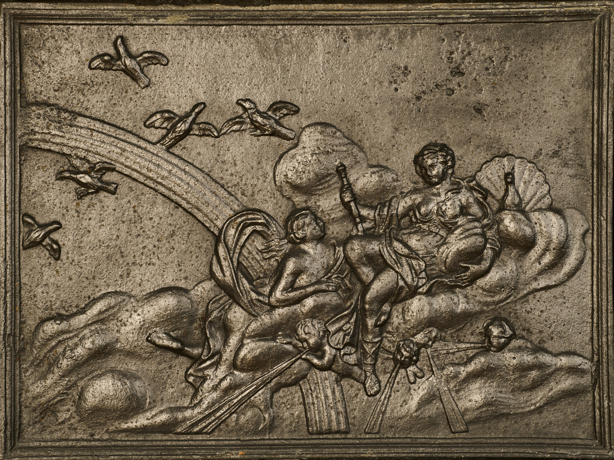 Ovn i to etasjer, utført i støpejern. Den bæres av en trebase med rokokkoornamentikk på midten av sargen, samt svungne capriolben. Samtlige sider er riflet, og innrammet av listverk og profiler. Frontpanelet på nedre del viser en fremstilling av Iris som overbringer et budskap til Juno, omgitt av skyer, regnbue og amoriner som blåser i trompeter. Til venstre flyver Junos gjess. Det høyre sidefeltet har ovnsluke og askebrett, kronet med en rokokkokartusj. Frontpanelet i andre etasje er gjennombrutt, og er dekorert med asymmetriske rocailler. Svakt fremtrukket toppstykke, som avsluttes med et sylinderformet ovnsrør med knekk som forbinder ovnen til brannmuren.