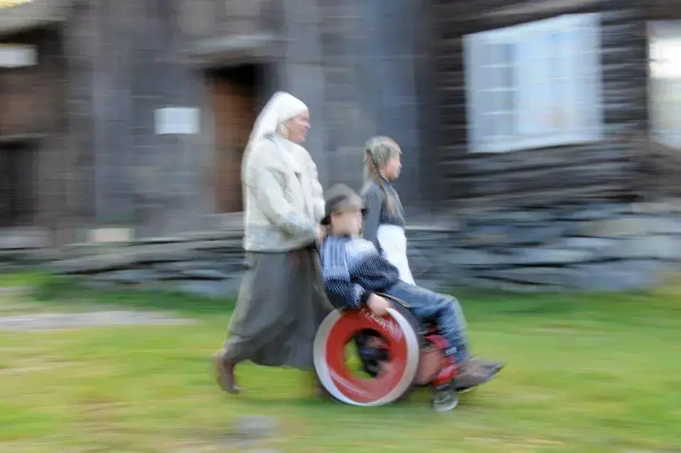 kvinne med kvitt hovudplagg som trillar ein gut i rullestol