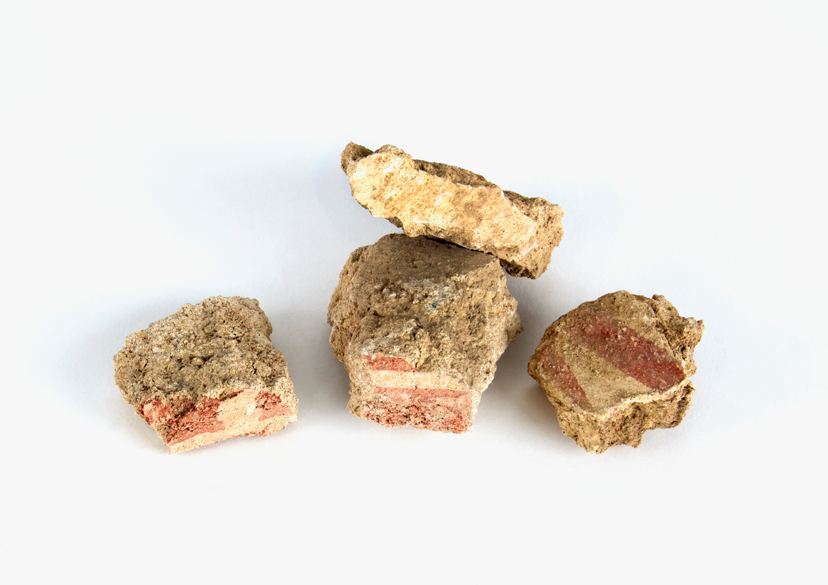 En samling av fragment av målad puts och bruk med kalkputs och bemålning. 17 fyndaskar med fragment i olika storlekar.

Fyndask 1: Totalt 13 fragment med röd och vit färg, en ser ut att ha träavtryck (varit fäst mot ett trästycke).

Fyndask 2: Totalt 7 fragment alla utom en har röd och vit färg, endast en med gråaktig obehandlad puts. 

Fyndask 3: Totalt 1 större fragment med röd och vit färg på enda sidan.

Fyndask 4: Totalt 4 fragment alla utom en med röd och vit färg, endast en med vit puts. 

Fyndask 5: Totalt 3 fragment med röd och vit färg, varav en är sotig. 

Fyndask 6: Totalt 3 fragment med röd och vit färg, en mycket tydlig medan de andra två mer diffusa. 

Fyndask 7:  Totalt 27 fragment, 24 av dessa är bemålade med röd och vit färg, 3  fragment med gråaktig obehandlad puts. 

Fyndask 8: Totalt 5 fragment, varav 4 större och en mycket liten. Alla större fragment med olika karaktär. En med vit kalkbruk och utan putsad yta, en annan med svart och röd putsad yta. Det tredje fragmentet har lite rödfärgad puts bevarad och på andra sidan ser det ut att ha träavtryck (varit fäst mot ett trästycke). Det fjärde fragmentet har en mer brungrå nyans. I fyndasken låg en lapp med text N. om V. portalen. 

Fyndask 9: Totalt 13 fragment, varav ett större fragment med svart och rödmålad puts. Ett annat fragment med svart och vitmålad puts, det tredje fragmentet har endast svartmålad puts. Sedan finns tre rödmålande putsfragment, samt tre fragment med röda linjer. Fyra fragment är ytterst små och intetsägande.

Fyndask 10: Totalt 9 fragment samt smådelar varav två har rött färgfragment. Det största fragmentet samt fyra andra är svart- och rödmålat. Tre putsfragment har röda linjer.
 
Fyndask 11: Totalt 1 fragment med röda linjer samt en mindre del med blågråa linjer. 

Fyndask 12: Totalt 1 fragment med blågrå rundad linje samt samt en mindre punkt eller koncentration nedanför.  

Fyndask 13: Totalt 5 fragment varav två med rödmålad puts. De andra tre har linjer. 

Fyndask 14: Totalt 1 fragment med vit och rödmålad puts, med flertal linjer som eventuellt kan vara del av en bokstav.
 
Fyndask 15: Totalt 1 fragment med vit och svartmålad puts, med flertal linjer som eventuellt kan vara del av en större figur. Ena delen syns en större koncentration som skulle kunna vara en fågel. 

Fyndask 16: Totalt 1 fragment med vit och rödmålad puts, med flertal rundade linjer som eventuellt kan vara del av växtlig dekor.

Fyndask 17: Totalt 1 fragment med rödmålad puts, med en vit linje.