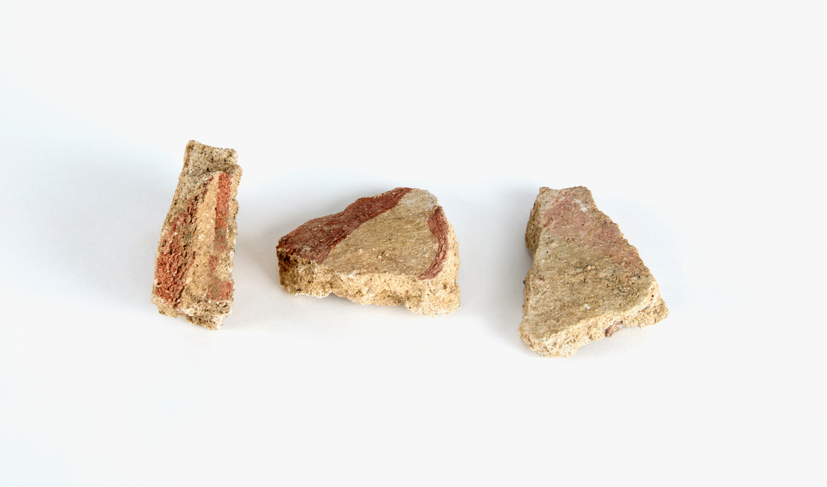 En samling av fragment av målad puts och bruk med kalkputs och bemålning. 17 fyndaskar med fragment i olika storlekar.

Fyndask 1: Totalt 13 fragment med röd och vit färg, en ser ut att ha träavtryck (varit fäst mot ett trästycke).

Fyndask 2: Totalt 7 fragment alla utom en har röd och vit färg, endast en med gråaktig obehandlad puts. 

Fyndask 3: Totalt 1 större fragment med röd och vit färg på enda sidan.

Fyndask 4: Totalt 4 fragment alla utom en med röd och vit färg, endast en med vit puts. 

Fyndask 5: Totalt 3 fragment med röd och vit färg, varav en är sotig. 

Fyndask 6: Totalt 3 fragment med röd och vit färg, en mycket tydlig medan de andra två mer diffusa. 

Fyndask 7:  Totalt 27 fragment, 24 av dessa är bemålade med röd och vit färg, 3  fragment med gråaktig obehandlad puts. 

Fyndask 8: Totalt 5 fragment, varav 4 större och en mycket liten. Alla större fragment med olika karaktär. En med vit kalkbruk och utan putsad yta, en annan med svart och röd putsad yta. Det tredje fragmentet har lite rödfärgad puts bevarad och på andra sidan ser det ut att ha träavtryck (varit fäst mot ett trästycke). Det fjärde fragmentet har en mer brungrå nyans. I fyndasken låg en lapp med text N. om V. portalen. 

Fyndask 9: Totalt 13 fragment, varav ett större fragment med svart och rödmålad puts. Ett annat fragment med svart och vitmålad puts, det tredje fragmentet har endast svartmålad puts. Sedan finns tre rödmålande putsfragment, samt tre fragment med röda linjer. Fyra fragment är ytterst små och intetsägande.

Fyndask 10: Totalt 9 fragment samt smådelar varav två har rött färgfragment. Det största fragmentet samt fyra andra är svart- och rödmålat. Tre putsfragment har röda linjer.
 
Fyndask 11: Totalt 1 fragment med röda linjer samt en mindre del med blågråa linjer. 

Fyndask 12: Totalt 1 fragment med blågrå rundad linje samt samt en mindre punkt eller koncentration nedanför.  

Fyndask 13: Totalt 5 fragment varav två med rödmålad puts. De andra tre har linjer. 

Fyndask 14: Totalt 1 fragment med vit och rödmålad puts, med flertal linjer som eventuellt kan vara del av en bokstav.
 
Fyndask 15: Totalt 1 fragment med vit och svartmålad puts, med flertal linjer som eventuellt kan vara del av en större figur. Ena delen syns en större koncentration som skulle kunna vara en fågel. 

Fyndask 16: Totalt 1 fragment med vit och rödmålad puts, med flertal rundade linjer som eventuellt kan vara del av växtlig dekor.

Fyndask 17: Totalt 1 fragment med rödmålad puts, med en vit linje.