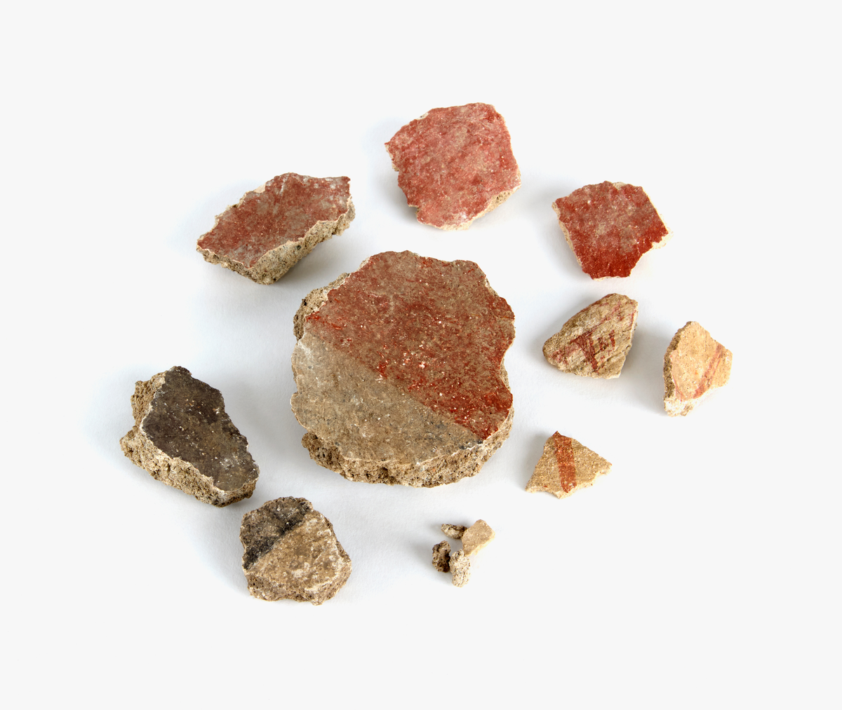 En samling av fragment av målad puts och bruk med kalkputs och bemålning. 17 fyndaskar med fragment i olika storlekar.

Fyndask 1: Totalt 13 fragment med röd och vit färg, en ser ut att ha träavtryck (varit fäst mot ett trästycke).

Fyndask 2: Totalt 7 fragment alla utom en har röd och vit färg, endast en med gråaktig obehandlad puts. 

Fyndask 3: Totalt 1 större fragment med röd och vit färg på enda sidan.

Fyndask 4: Totalt 4 fragment alla utom en med röd och vit färg, endast en med vit puts. 

Fyndask 5: Totalt 3 fragment med röd och vit färg, varav en är sotig. 

Fyndask 6: Totalt 3 fragment med röd och vit färg, en mycket tydlig medan de andra två mer diffusa. 

Fyndask 7:  Totalt 27 fragment, 24 av dessa är bemålade med röd och vit färg, 3  fragment med gråaktig obehandlad puts. 

Fyndask 8: Totalt 5 fragment, varav 4 större och en mycket liten. Alla större fragment med olika karaktär. En med vit kalkbruk och utan putsad yta, en annan med svart och röd putsad yta. Det tredje fragmentet har lite rödfärgad puts bevarad och på andra sidan ser det ut att ha träavtryck (varit fäst mot ett trästycke). Det fjärde fragmentet har en mer brungrå nyans. I fyndasken låg en lapp med text N. om V. portalen. 

Fyndask 9: Totalt 13 fragment, varav ett större fragment med svart och rödmålad puts. Ett annat fragment med svart och vitmålad puts, det tredje fragmentet har endast svartmålad puts. Sedan finns tre rödmålande putsfragment, samt tre fragment med röda linjer. Fyra fragment är ytterst små och intetsägande.

Fyndask 10: Totalt 9 fragment samt smådelar varav två har rött färgfragment. Det största fragmentet samt fyra andra är svart- och rödmålat. Tre putsfragment har röda linjer.
 
Fyndask 11: Totalt 1 fragment med röda linjer samt en mindre del med blågråa linjer. 

Fyndask 12: Totalt 1 fragment med blågrå rundad linje samt samt en mindre punkt eller koncentration nedanför.  

Fyndask 13: Totalt 5 fragment varav två med rödmålad puts. De andra tre har linjer. 

Fyndask 14: Totalt 1 fragment med vit och rödmålad puts, med flertal linjer som eventuellt kan vara del av en bokstav.
 
Fyndask 15: Totalt 1 fragment med vit och svartmålad puts, med flertal linjer som eventuellt kan vara del av en större figur. Ena delen syns en större koncentration som skulle kunna vara en fågel. 

Fyndask 16: Totalt 1 fragment med vit och rödmålad puts, med flertal rundade linjer som eventuellt kan vara del av växtlig dekor.

Fyndask 17: Totalt 1 fragment med rödmålad puts, med en vit linje.