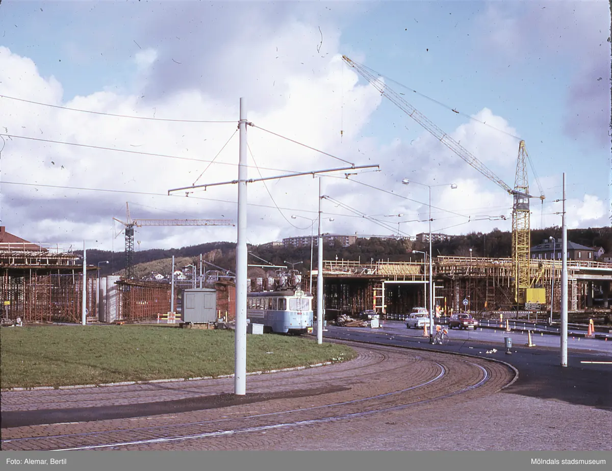 Långt framskriden byggnation av Mölndals bro, ser ut att vara taget under någon gång i slutet på våren eller i början av sommarmånaderna juni till augusti.
Tid: Cirka början av 1970-talet. 
Bilden visar stadstrafik samt anläggningsarbete.  
I fokus skymtar spårgvagnsspåren och del av den gamla vändslingan för spårvagnen, innan den blir överbyggd.

Till vänster i bild skymtar taket till Hantverkshuset, bakom byggnadsställningen.