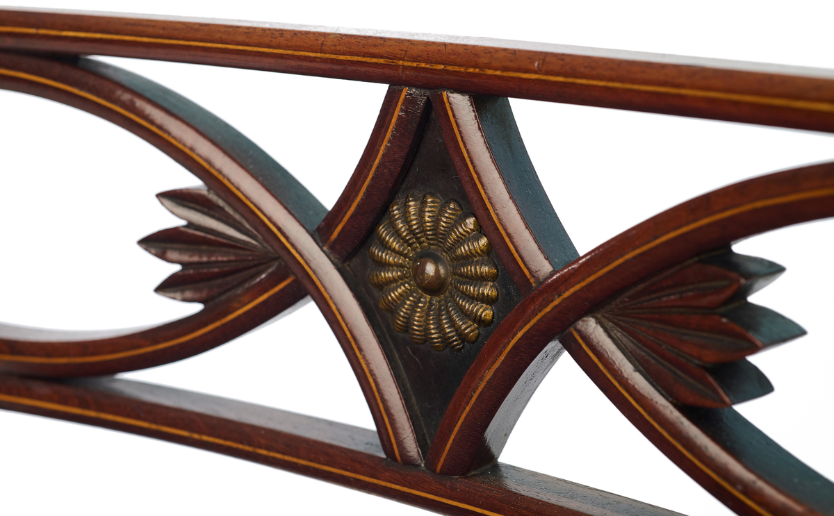 Stol av finért mahogni, som hviler på fire ben. Åpen rygg med glatt buet toppstykke med intarsia i lyst tre. Gjennombrutt tverrspross med halvsirkelformede ornamenter, hvor det ovale midtpartiet er markert med en riflet metallrosett. Kurvede akterstaver glir over i bakbenene, mens forbenene er dreide. Trapesformet sete med sekundært blåfarget trekk i ull. Mykt buet sarg, hvis sider er svakt trukket inn under setet.
