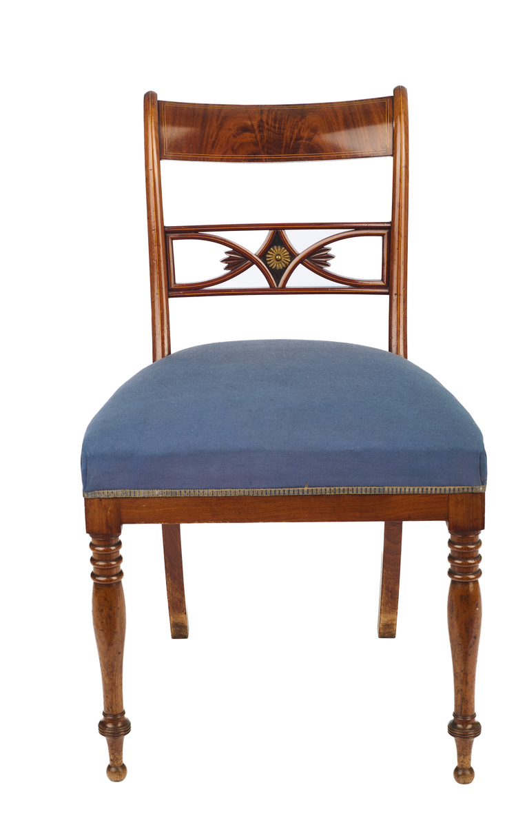 Stol av finért mahogni, som hviler på fire ben. Åpen rygg med glatt buet toppstykke med intarsia i lyst tre. Gjennombrutt tverrspross med halvsirkelformede ornamenter, hvor det ovale midtpartiet er markert med en riflet metallrosett. Kurvede akterstaver glir over i bakbenene, mens forbenene er dreide. Trapesformet sete med sekundært blåfarget trekk i ull. Mykt buet sarg, hvis sider er svakt trukket inn under setet.