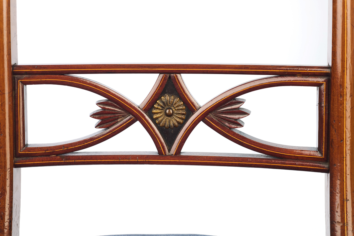 Stol av finért mahogni, som hviler på fire ben. Åpen rygg med glatt buet toppstykke med intarsia i lyst tre. Gjennombrutt tverrspross med halvsirkelformede ornamenter, hvor det ovale midtpartiet er markert med en riflet metallrosett. Kurvede akterstaver glir over i bakbenene, mens forbenene er dreide. Trapesformet sete med sekundært blåfarget trekk i ull. Mykt buet sarg, hvis sider er svakt trukket inn under setet.