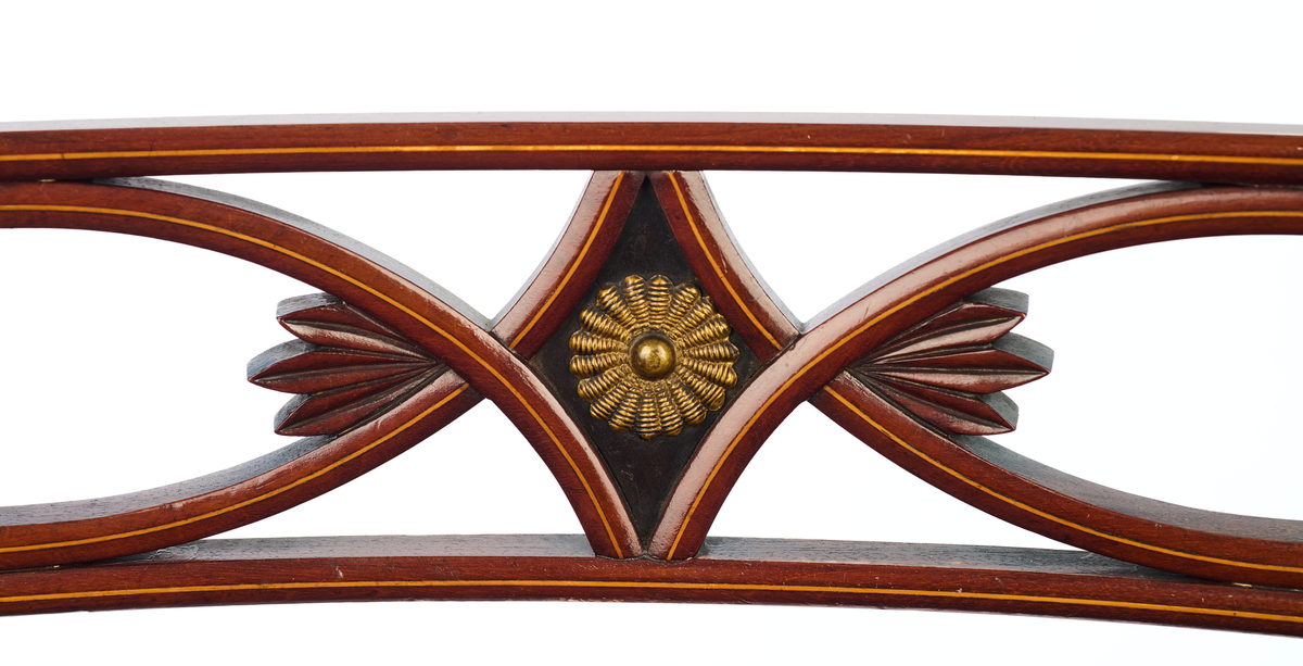 Stol av finért mahogni, som hviler på fire ben. Åpen rygg med glatt buet toppstykke med intarsia i lyst tre. Gjennombrutt tverrspross med halvsirkelformede ornamenter, hvor det ovale midtpartiet er markert med en riflet metallrosett. Kurvede akterstaver glir over i bakbenene, mens forbenene er dreide. Trapesformet sete med sekundært blåfarget trekk i ull. Mykt buet sarg, hvis sider er svakt trukket inn under setet.