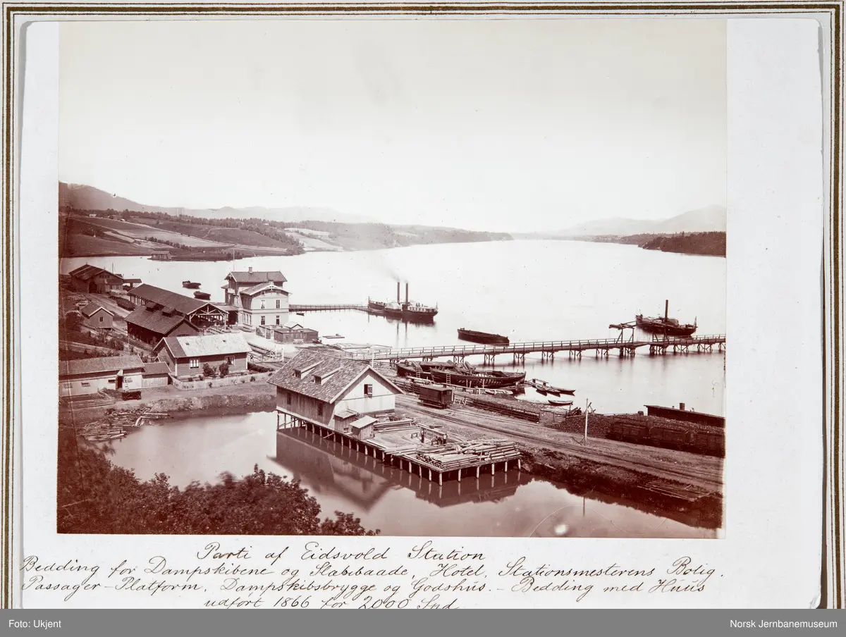 Oversiktsbilde med Eidsvoll stasjon, to dampbåter, beddingen med to klinkbygde lektere og brua over Vorma