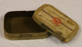 Tobakkseske. Papp med etikett i gult papir på lokk. Rektangulær med avrundede kanter. Brun og hvit skrift. Hvit bulldog med rød sirkulær bakgrunn. 