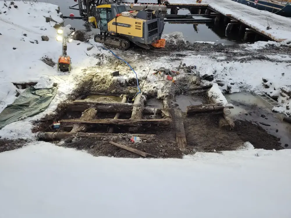 Trästockar, snö och grävmaskin