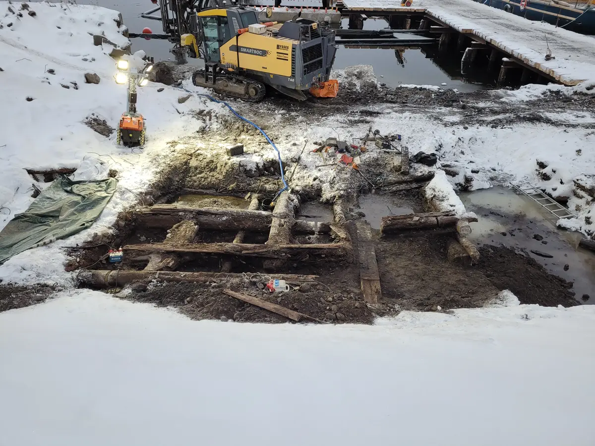 Trästockar, snö och grävmaskin