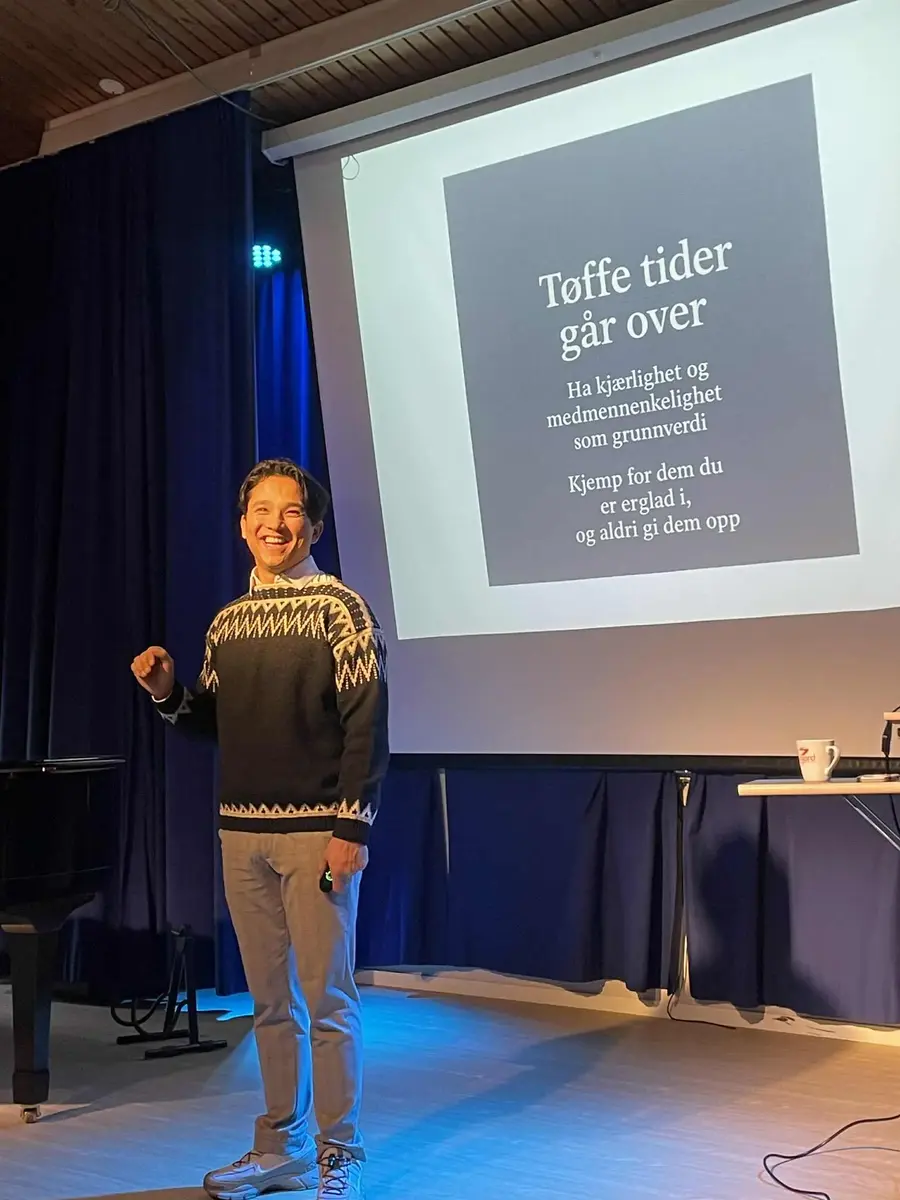 En smilende mann står foran en skjerm med tittel Tøffe tider går over.