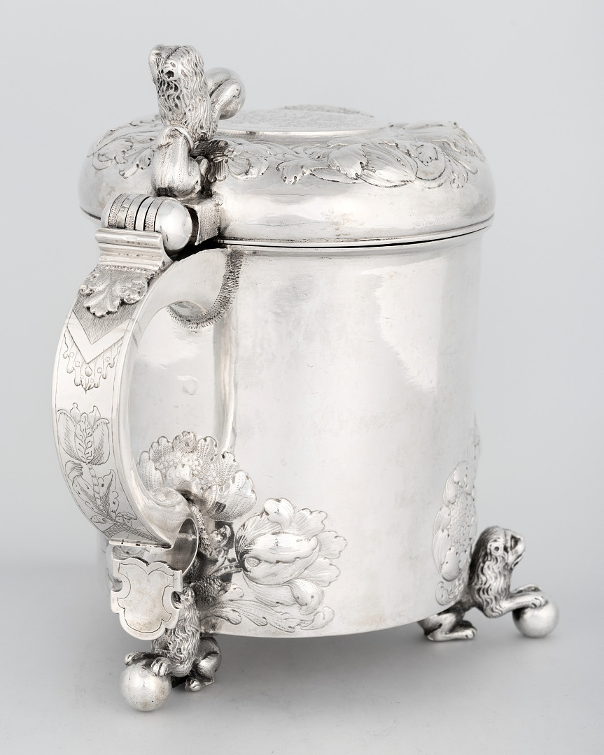 Drikkekanne i sølv. Sylindrisk korpus med drevet og siselert dekor, samt graverte innskrifter og motiver. De tre føttene har form av liggende løver med kule. Korpus og lokk er dekorert med drevet blomsterdekor nær ansatsene mot føttene. Sirkulært lokk, som har et hevet midtparti med speilmonogram. Lokkåpneren er utformet som en løve som står på bakbenene og støtter en forlabb på lokket og på en glatt kule. Buet hank som har et støpt blad øverst, deretter gravert blomsterdekor, og avsluttes av et skjold. Innvendig i sylinderen er det seks perler.