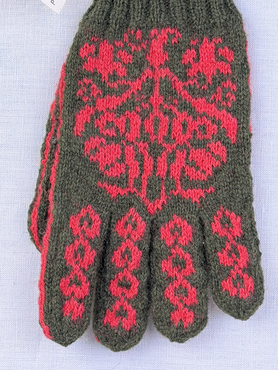 En stickad fingervante, med randig mudd i 2-2 resår (2 räta och 2 aviga maskor) och mönsterstickad vante i slätstickning, av 2-trådigt ullgarn.