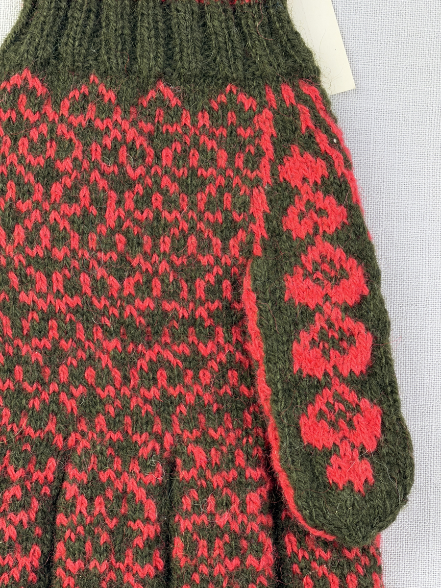 En stickad fingervante, med randig mudd i 2-2 resår (2 räta och 2 aviga maskor) och mönsterstickad vante i slätstickning, av 2-trådigt ullgarn.