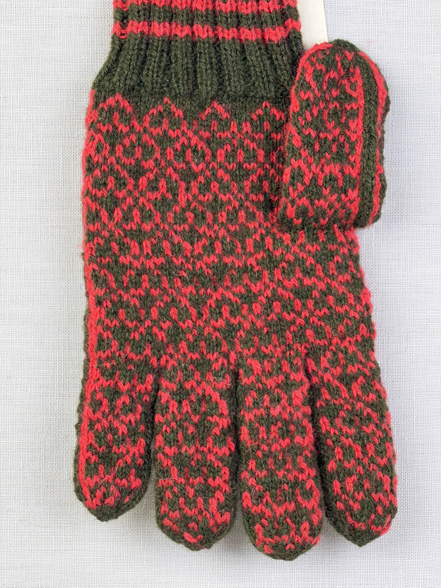 En stickad fingervante, med randig mudd i 2-2 resår (2 räta och 2 aviga maskor) och mönsterstickad vante i slätstickning, av 2-trådigt ullgarn.