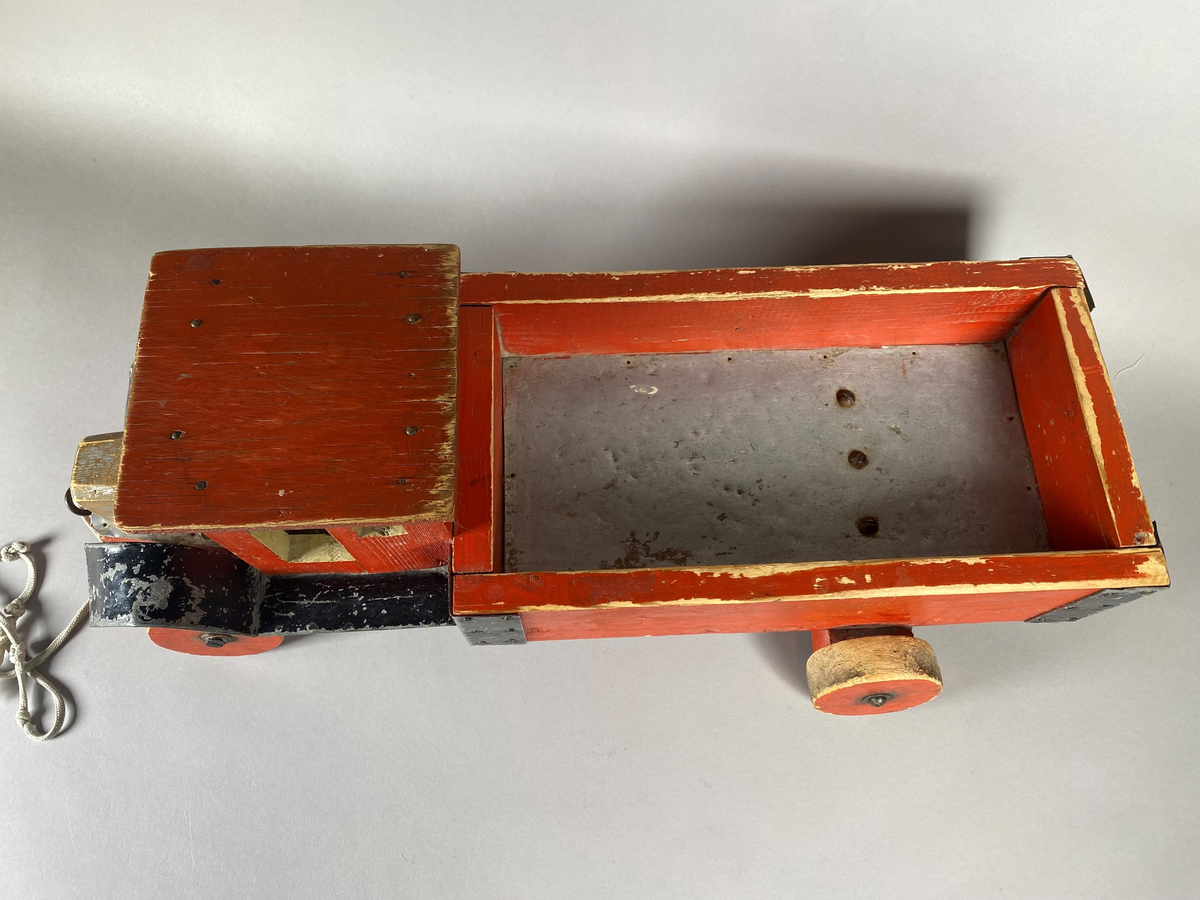 Lastebil snekret i tre med metallbeslag. Treverket er rødmalt, med svarte beslag. Lekebilen har to nummerskilt foran og bak med merking "U54227". På undersiden er gjenstanden merket med et påskrevet navn. På ene siden av lasteplanet er det festet et merke med Postverkets logomerke. Lekebilen har noe slitasjemerker, trolig etter bruk.