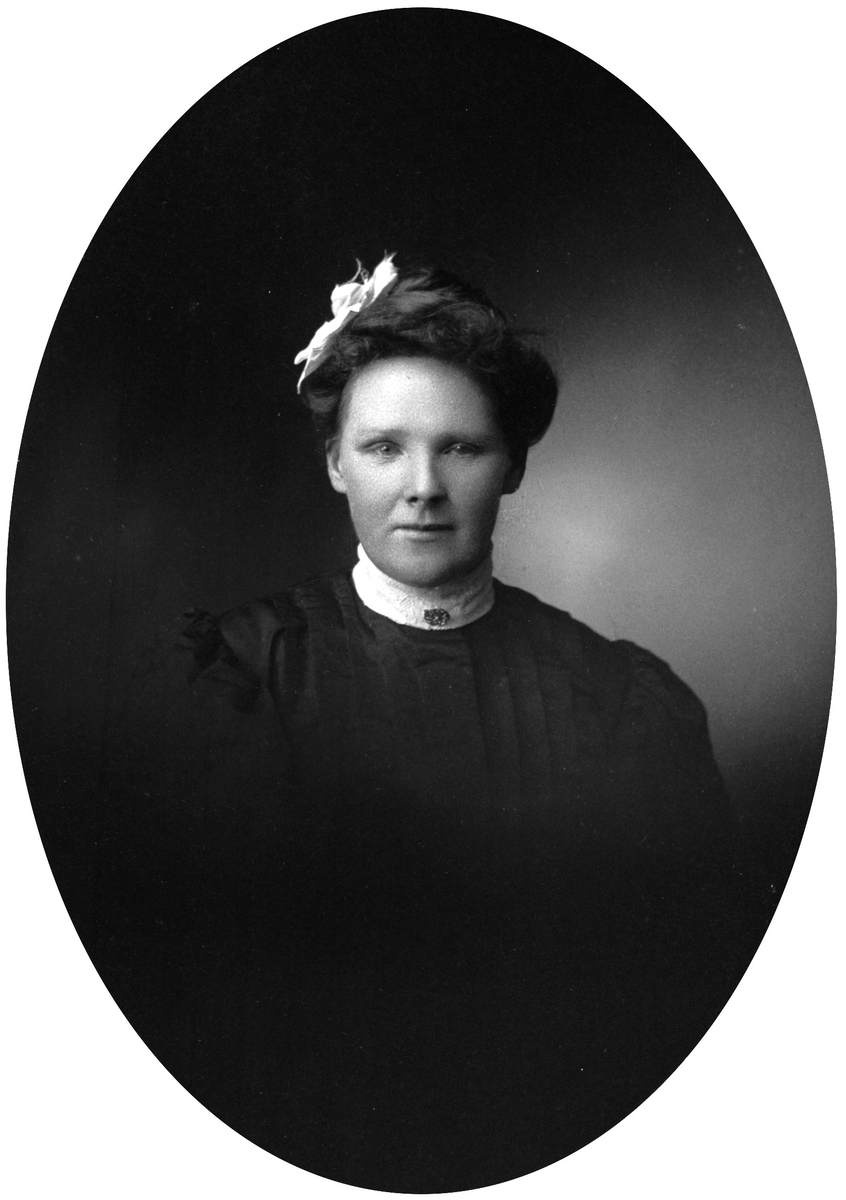 Portrett av en kvinne med mørkt hår med hvit sløyfe i. Påskrift bakpå: Thea Windingland