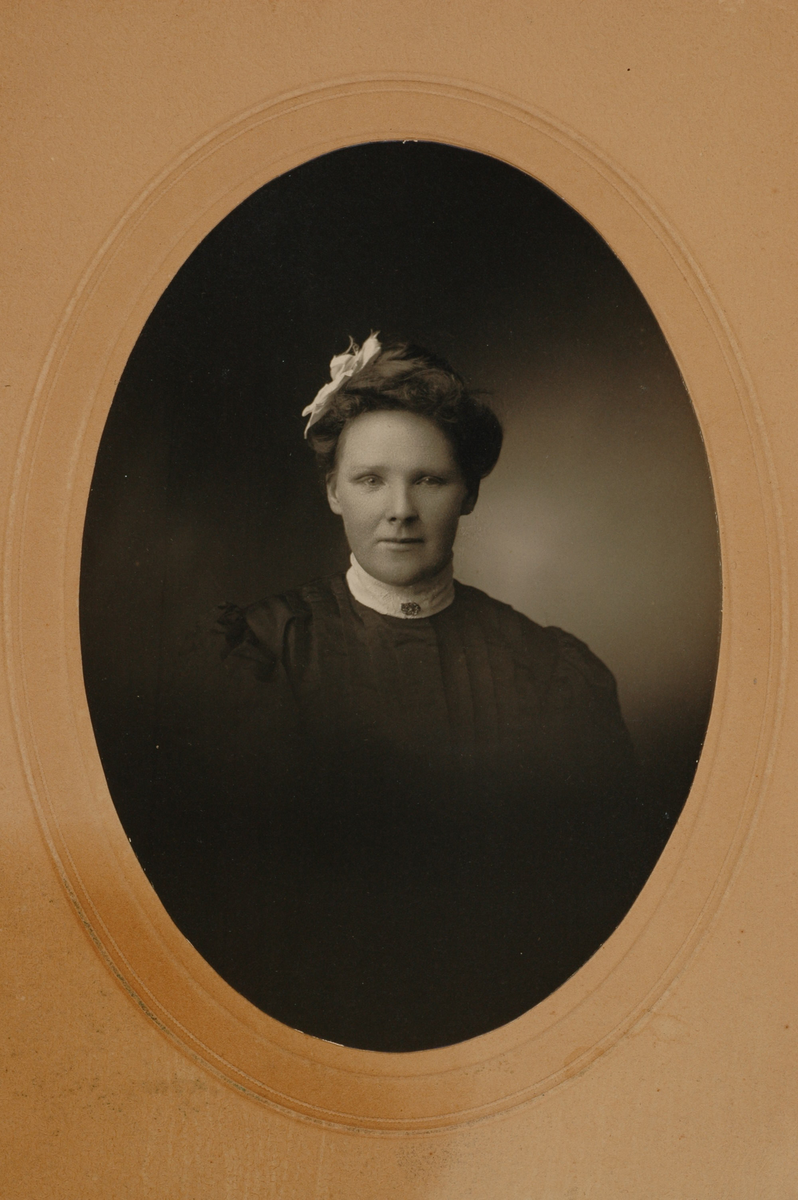 Portrett av en kvinne med mørkt hår med hvit sløyfe i. Påskrift bakpå: Thea Windingland